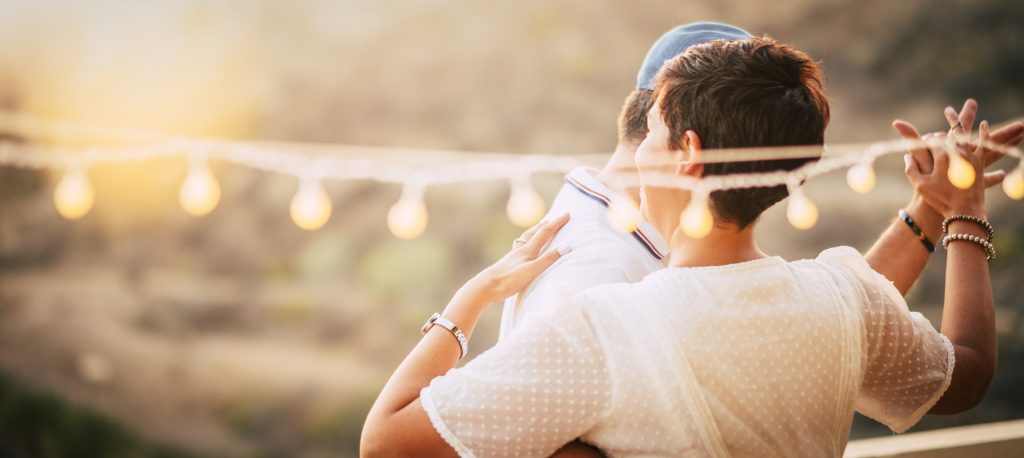 happy caucasian people dancing together at home in terrace with lights during the sunset. romantic and relationship concept image for happy people in outdoor leisure activity about love. warm and gold colors